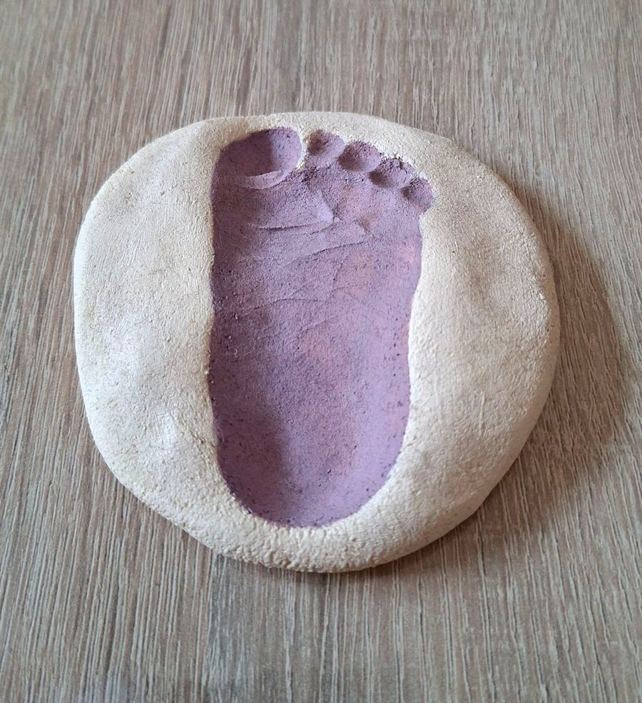 Fußabdruck eines Kindes in lila Farbe auf einem runden Stück Salzteig, fotografiert auf einem Holztisch